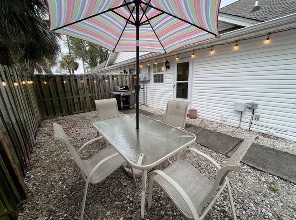 Une terrasse avec une table et des chaises en verre, un parasol à rayures et une clôture en bois.