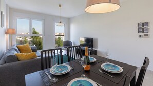 A dining area with a table set for two, a sofa with a yellow pillow, and a TV in the background. - Bright, Immaculate apartment in the Estepona port (Estepona)