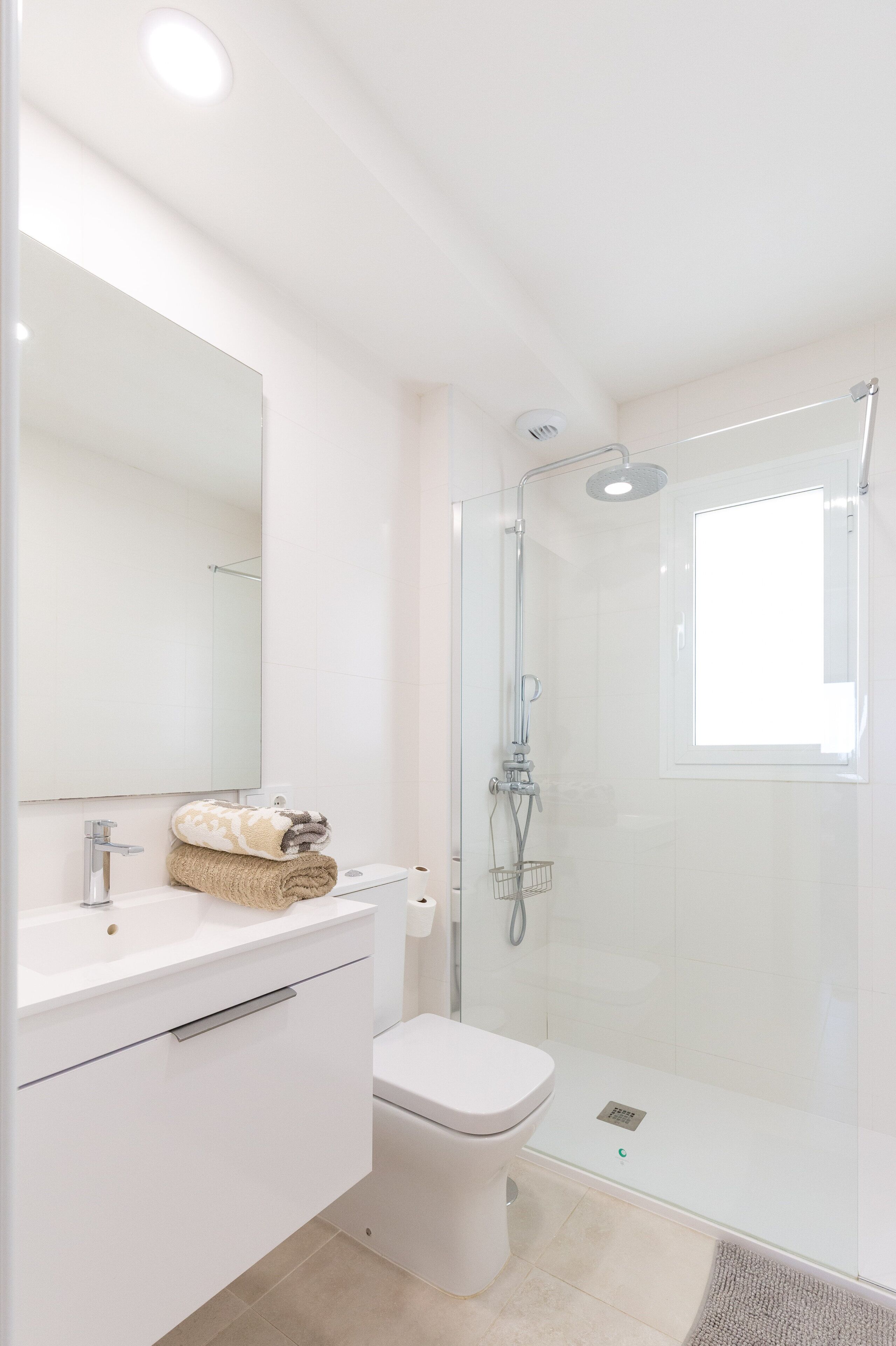 Een moderne badkamer met een glazen douchecabine, een witte wastafel en een toilet.