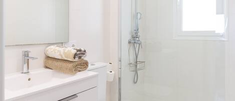 Een moderne badkamer met een glazen douchecabine, een witte wastafel en een toilet.