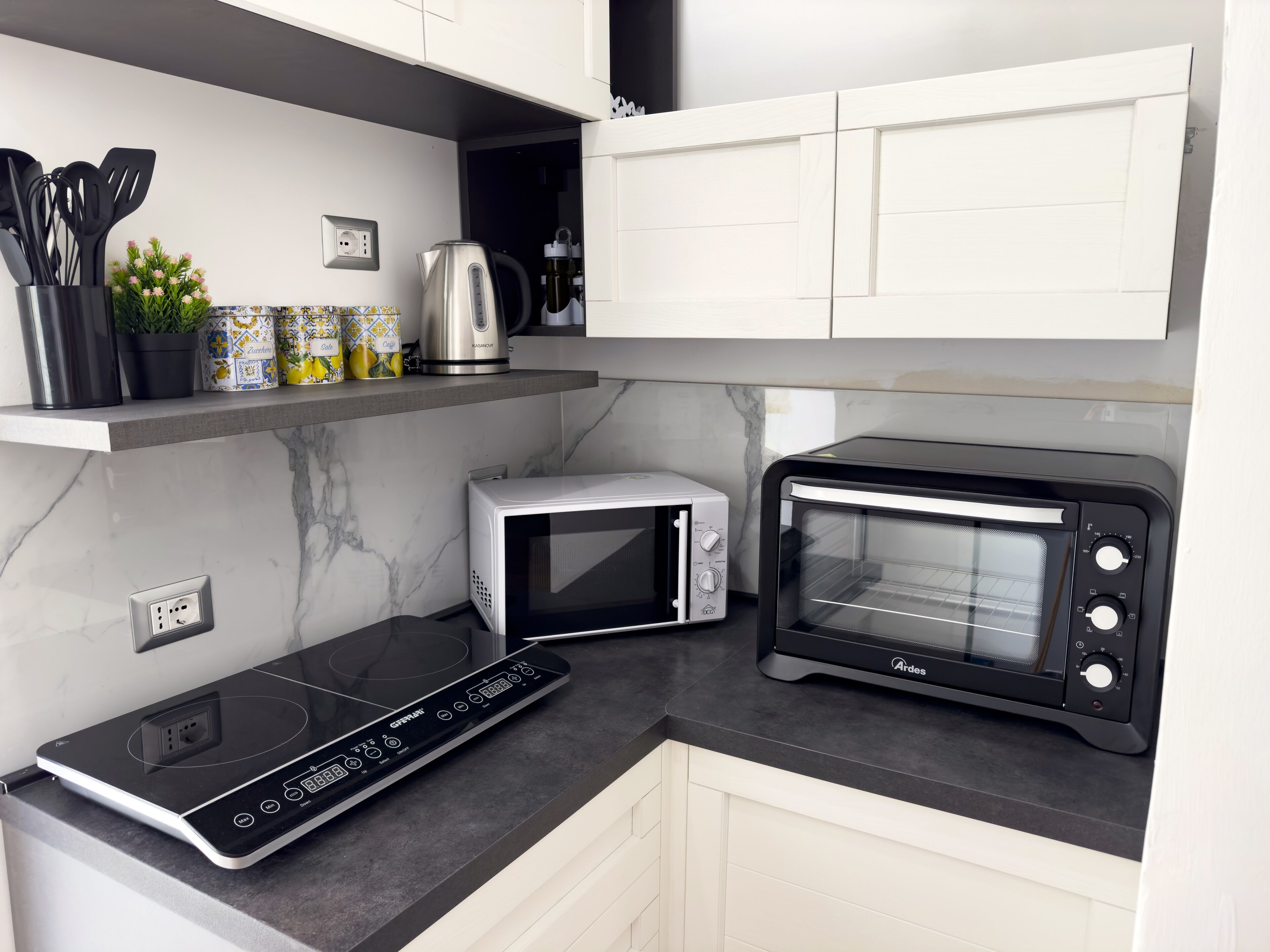 A modern kitchen with a built-in induction cooktop, a black toaster oven, a white microwave, and a coffee maker on a shelf.