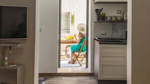 A modern kitchen with a built-in oven, a dining area with a table and chairs, and a TV mounted on the wall. - Syraka Courtyard - Apartment Ortigia Wifi (Siracusa)