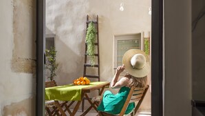 A dining area with a table set for two, a ladder with plants, and a window with a view. - Syraka Courtyard - Apartment Ortigia Wifi (Siracusa)