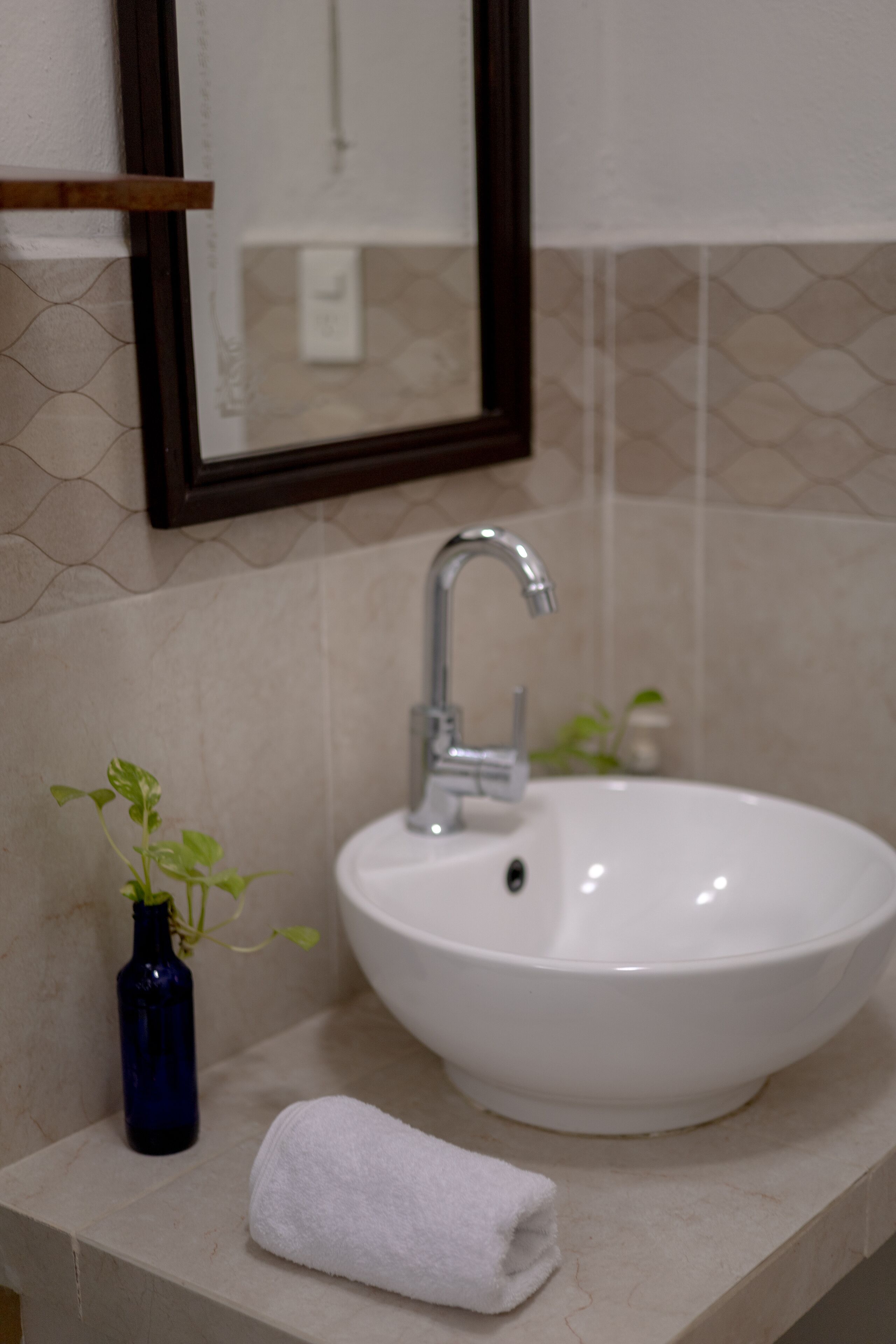 Ein Badezimmer mit einem weißen Waschbecken, einem Spiegel und einer kleinen blauen Vase mit Pflanze.