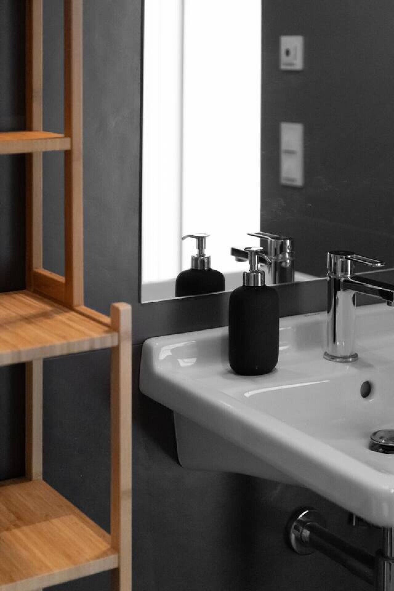 A bathroom with a white sink, a black soap dispenser, and a chrome faucet.