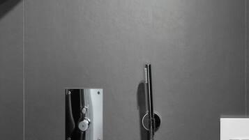 A shower with a handheld showerhead and a wall-mounted control panel.