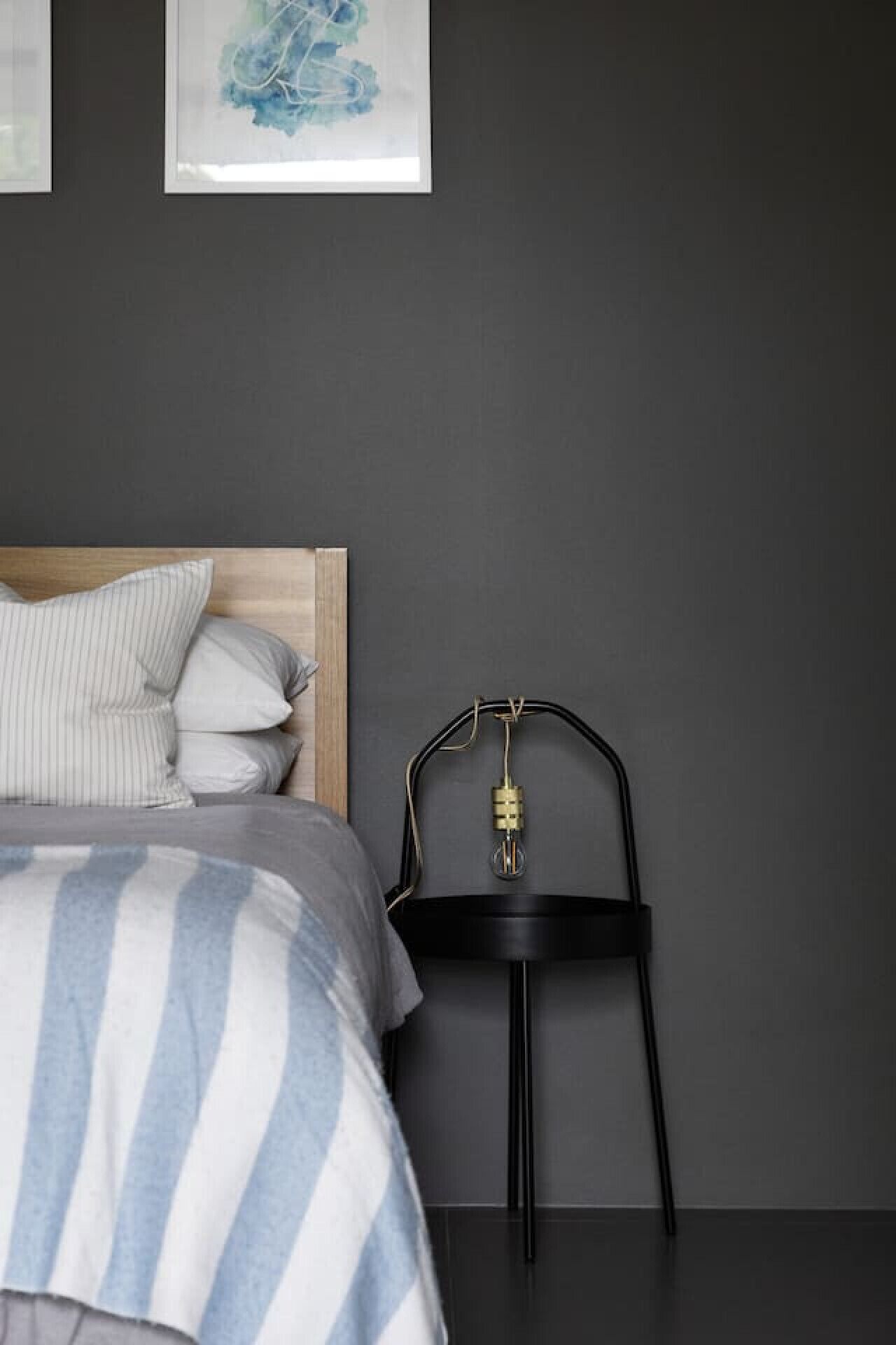 A bedroom with a bed, pillows, a bedside table with a lamp, and a wall with a framed picture.