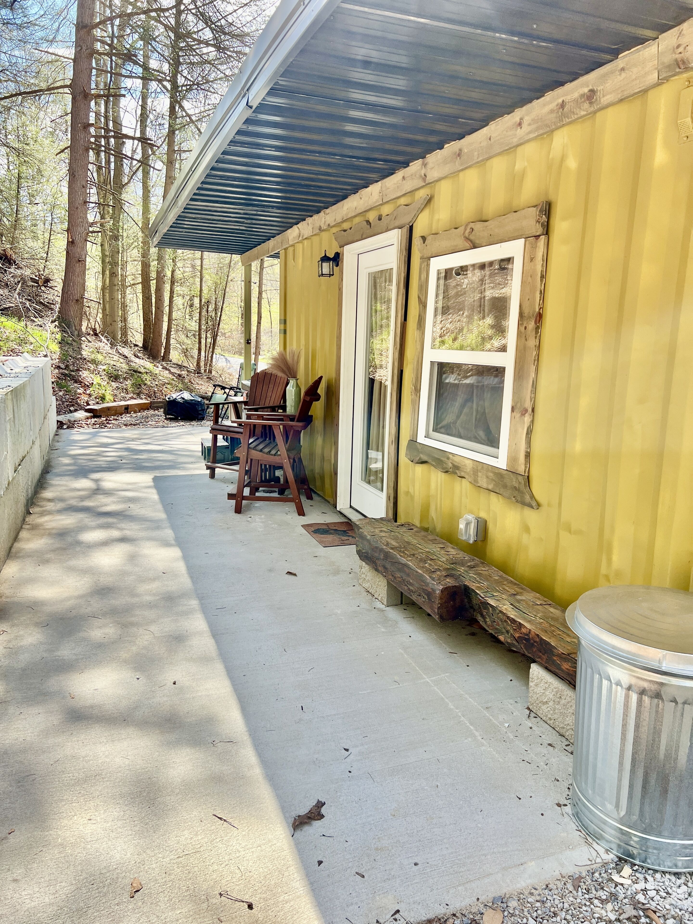 Eine gelbe Holzhütte mit überdachter Veranda, einer Holzbank und einem Mülleimer.