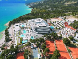 An aerial view of a coastal hotel with multiple swimming pools, tennis courts, and a beach area.