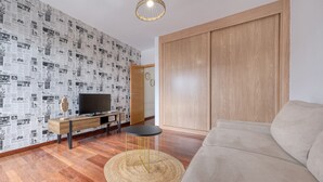 Un salon moderne avec un plancher en bois, un canapé, un téléviseur posé sur une console en bois et un papier peint à motifs.