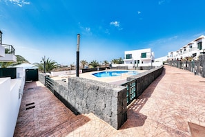 Un área de piscina en la azotea con un muro de piedra, cielo azul despejado y edificios blancos al fondo.