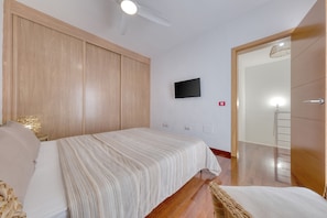 Quarto com cama, televisão na parede e guarda-roupa de madeira.