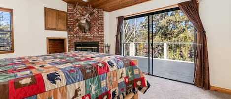Un dormitorio con una cama grande, chimenea y balcón con vistas a árboles.