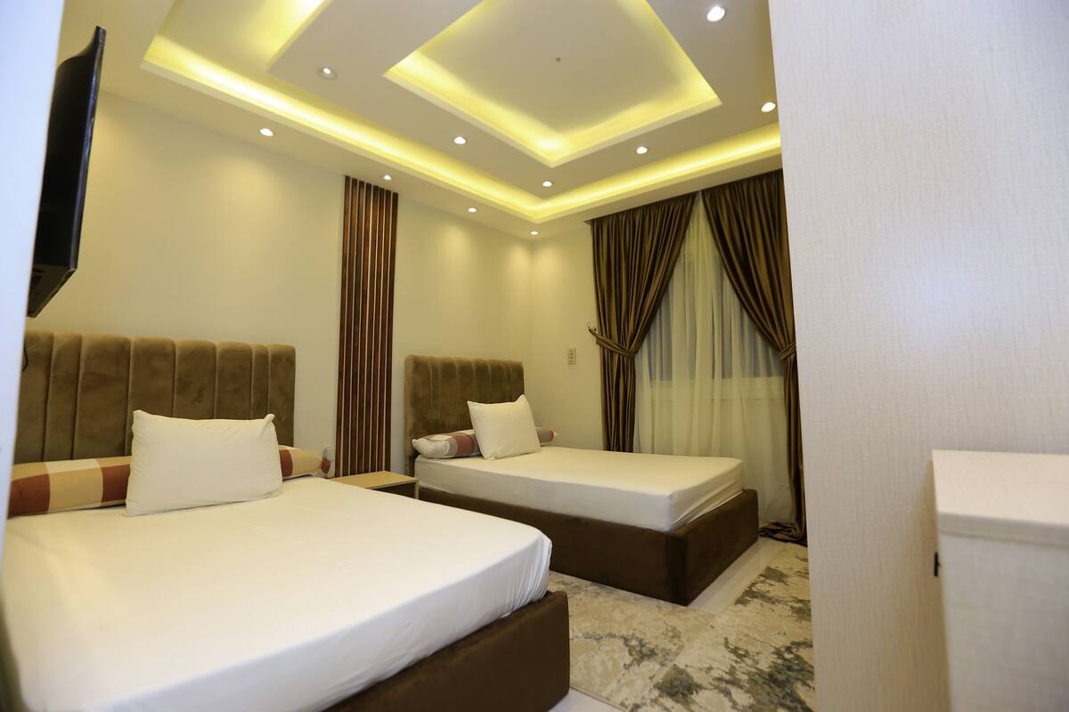 A hotel room with two beds, a flat-screen TV mounted on the wall, and a ceiling with recessed lighting.