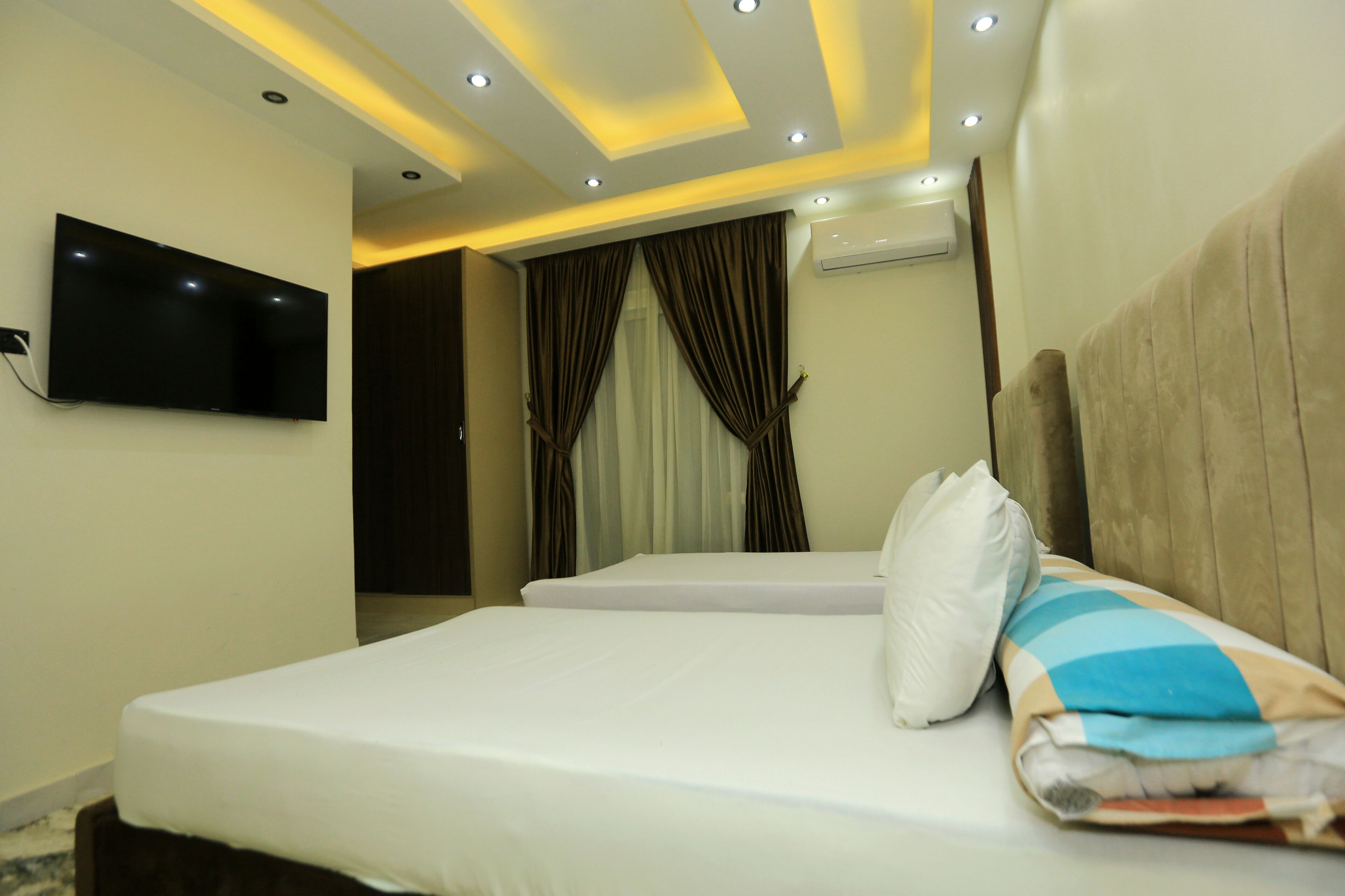 A hotel room with a bed, a flat-screen TV mounted on the wall, and a ceiling with recessed lighting.