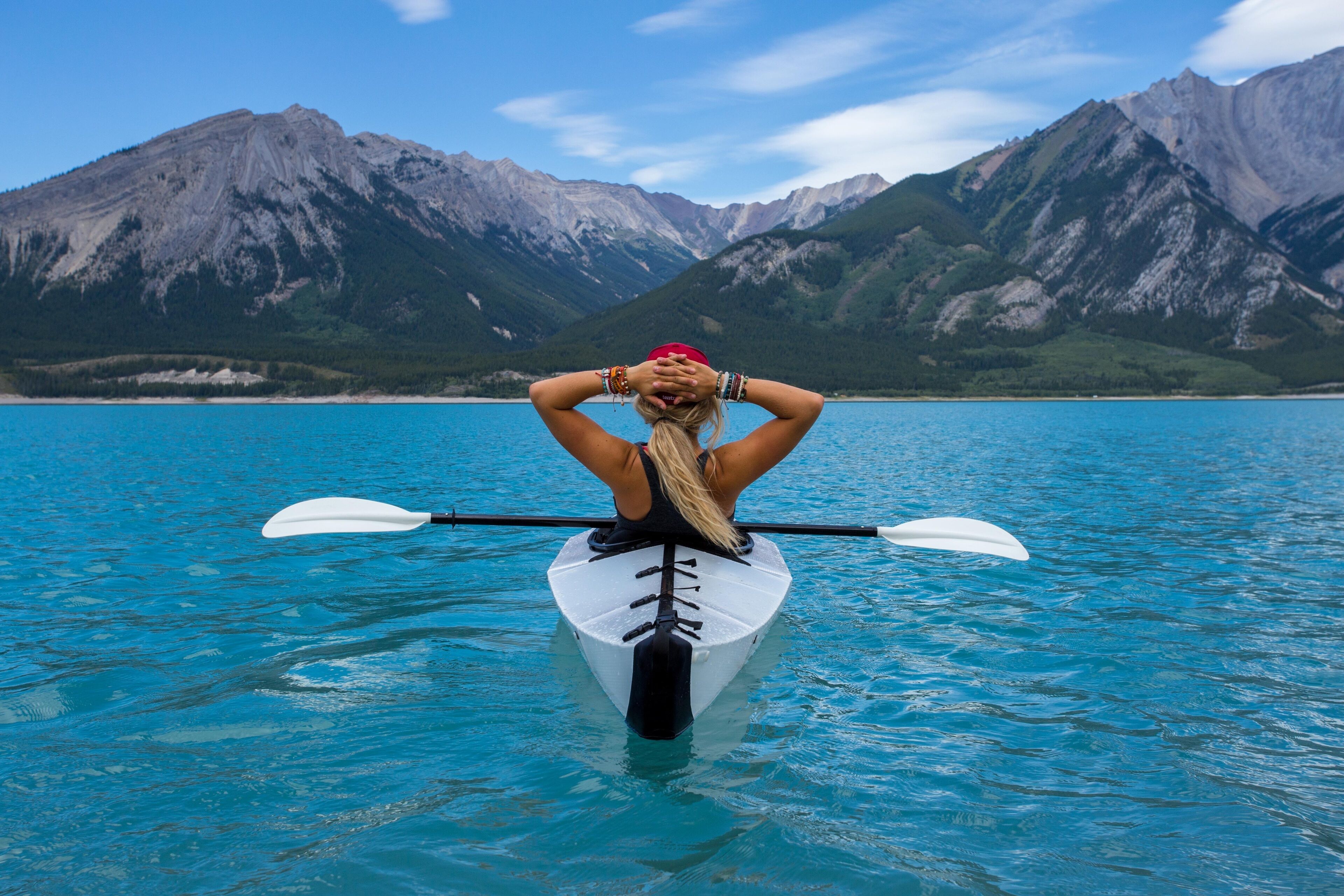 A person kayaking on a calm lake with mountains in the background.