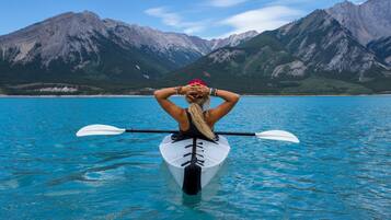 A person kayaking on a calm lake with mountains in the background.