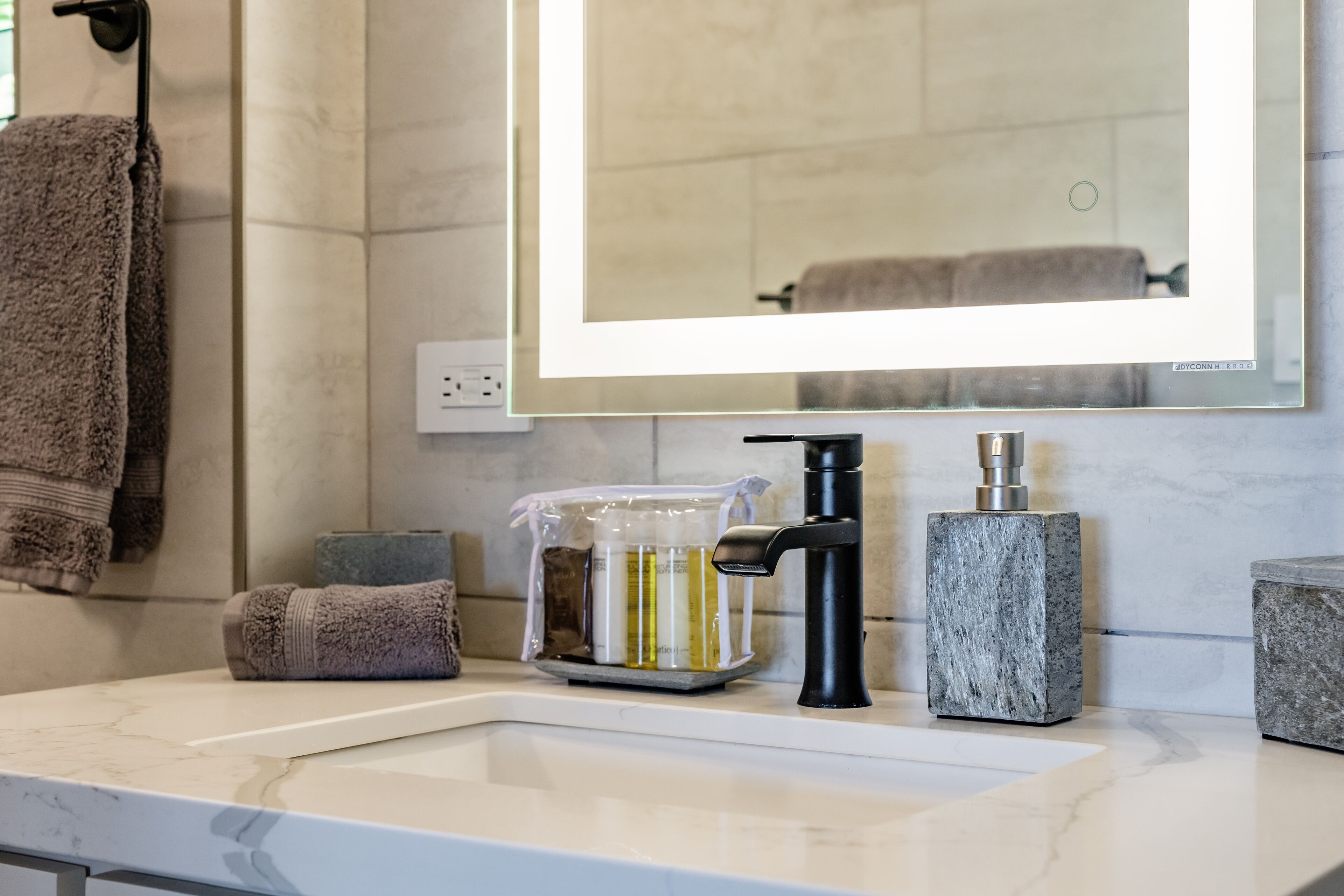 A bathroom with a white marble sink, a black faucet, a marble soap dispenser, and a glass container with soap and lotion.