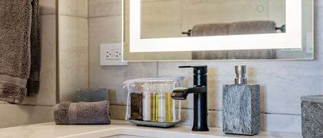 A bathroom with a white marble sink, a black faucet, a marble soap dispenser, and a glass container with soap and lotion.