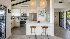 A modern kitchen with white cabinets, stainless steel appliances, and a large island with bar stools. - Upscale and Elegant Vistas (Kihei)