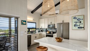 A modern kitchen with white cabinets, a large island, and a view to the outside. - Upscale and Elegant Vistas (Kihei)