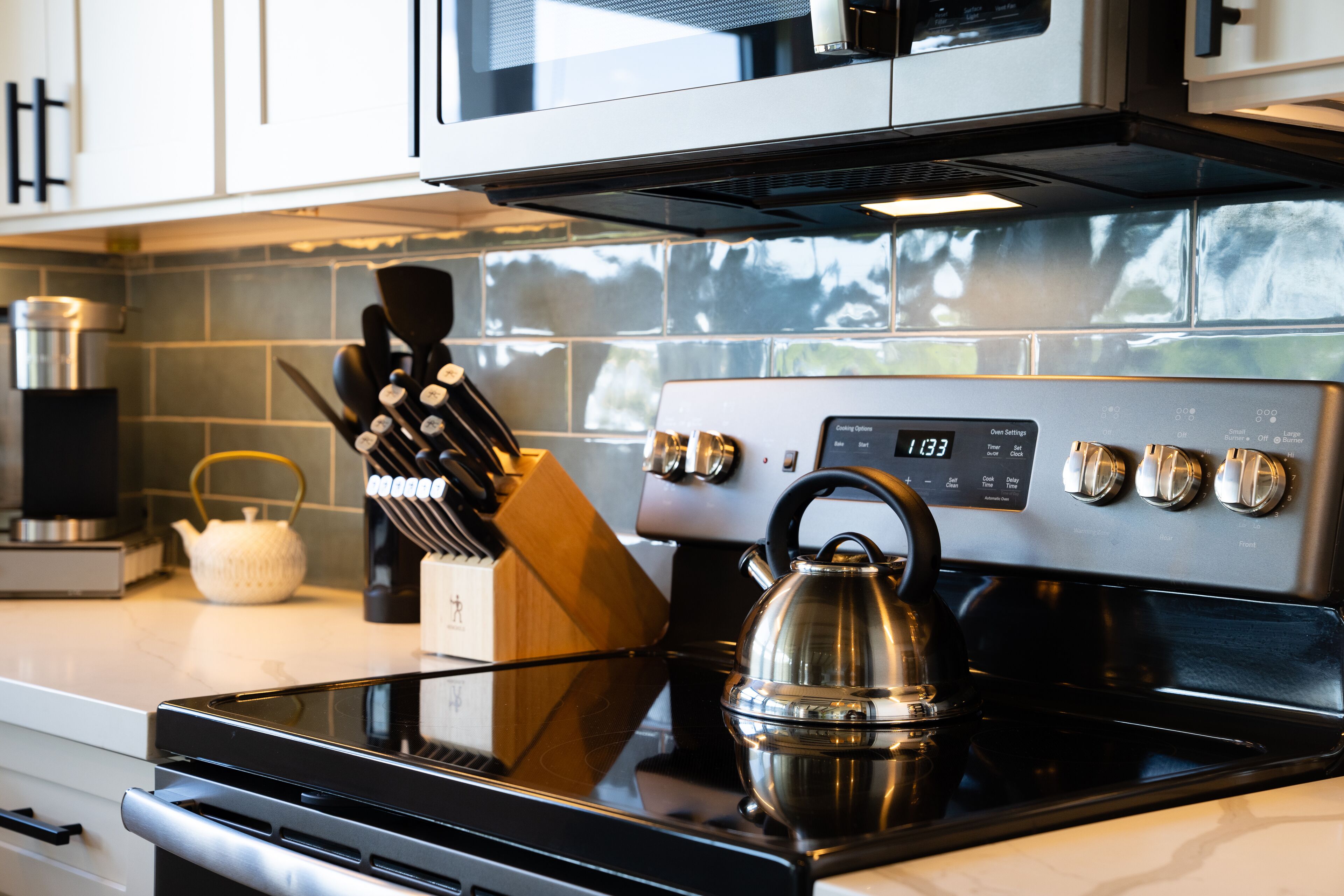 A modern kitchen with a stainless steel stove, a kettle, and a knife block.
