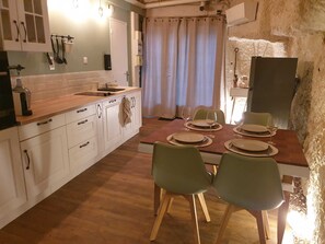 Ein Essbereich mit einem Holztisch, gedeckt für vier Personen, weißen Schränken und einer Küche mit an der Wand hängenden Küchenutensilien.