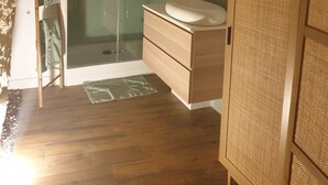 Ein Badezimmer mit einer gläsernen Duschkabine, Holzschränken und einem grünen Handtuchhalter.
