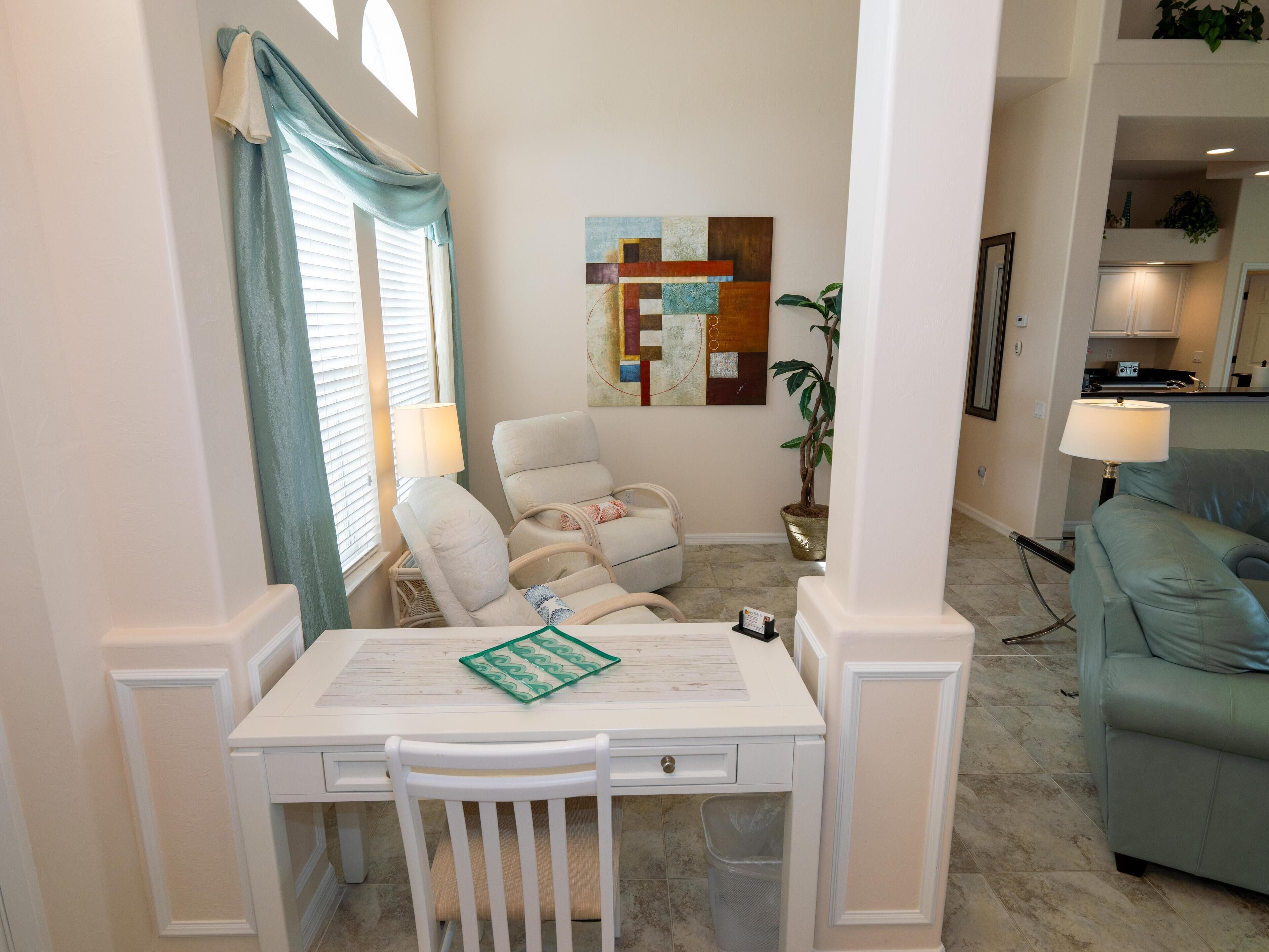 A dining area with a white table and chairs, a potted plant, and a painting on the wall.