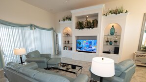 Un salon moderne avec un canapé d’angle, une table basse et un téléviseur fixé au mur, qui est de couleur blanche.