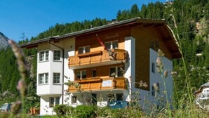 A multi-story building with balconies, surrounded by greenery and a mountainous backdrop. - Amaryllis by Interhome (Saas-Grund)