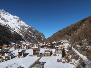 Ein verschneites Bergdorf mit traditionellen Holzhäusern, einer Seilbahn und wolkenlosem, blauem Himmel.