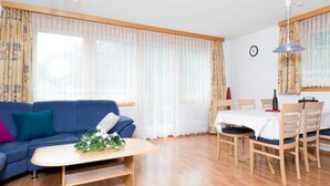 A living room with a blue sofa, a wooden coffee table, and a dining area with a table and chairs. - Amaryllis by Interhome (Saas-Grund)