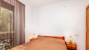 Ein Schlafzimmer mit einem Bett, zwei Nachttischen mit Lampen, einem Holzschrank und einem Fenster mit Vorhängen.