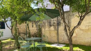 En terrasse med et bord, stole, en grøn parasol og et træ.