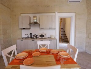 Cocina compacta con armarios blancos, microondas y tostadora. Una mesa de comedor con manteles individuales anaranjados y platos blancos dispuesta para cuatro comensales.