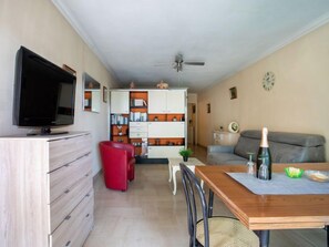 Una sala de estar con televisor, una butaca roja, una mesa de comedor de madera y un sofá.