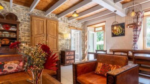 Una habitación acogedora con pared de piedra, vigas de madera en el techo, un sofá de cuero, una mesa de madera y un florero con flores.
