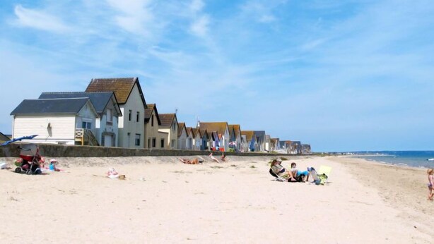 Una playa con casas al fondo y gente relajándose en la arena.