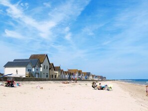 Una playa con casas al fondo y gente relajándose en la arena.