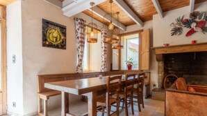 Una mesa de madera para comer con bancos, una chimenea y un ventanal con cortinas.