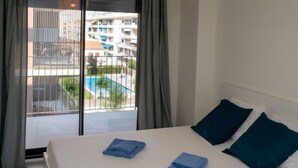 Ein Hotelzimmer mit einem Bett, zwei blauen Handtüchern und Blick auf einen Swimmingpool sowie Gebäude.