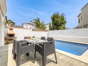 Um pátio externo com piscina, mesa posta para refeições e churrasqueira.