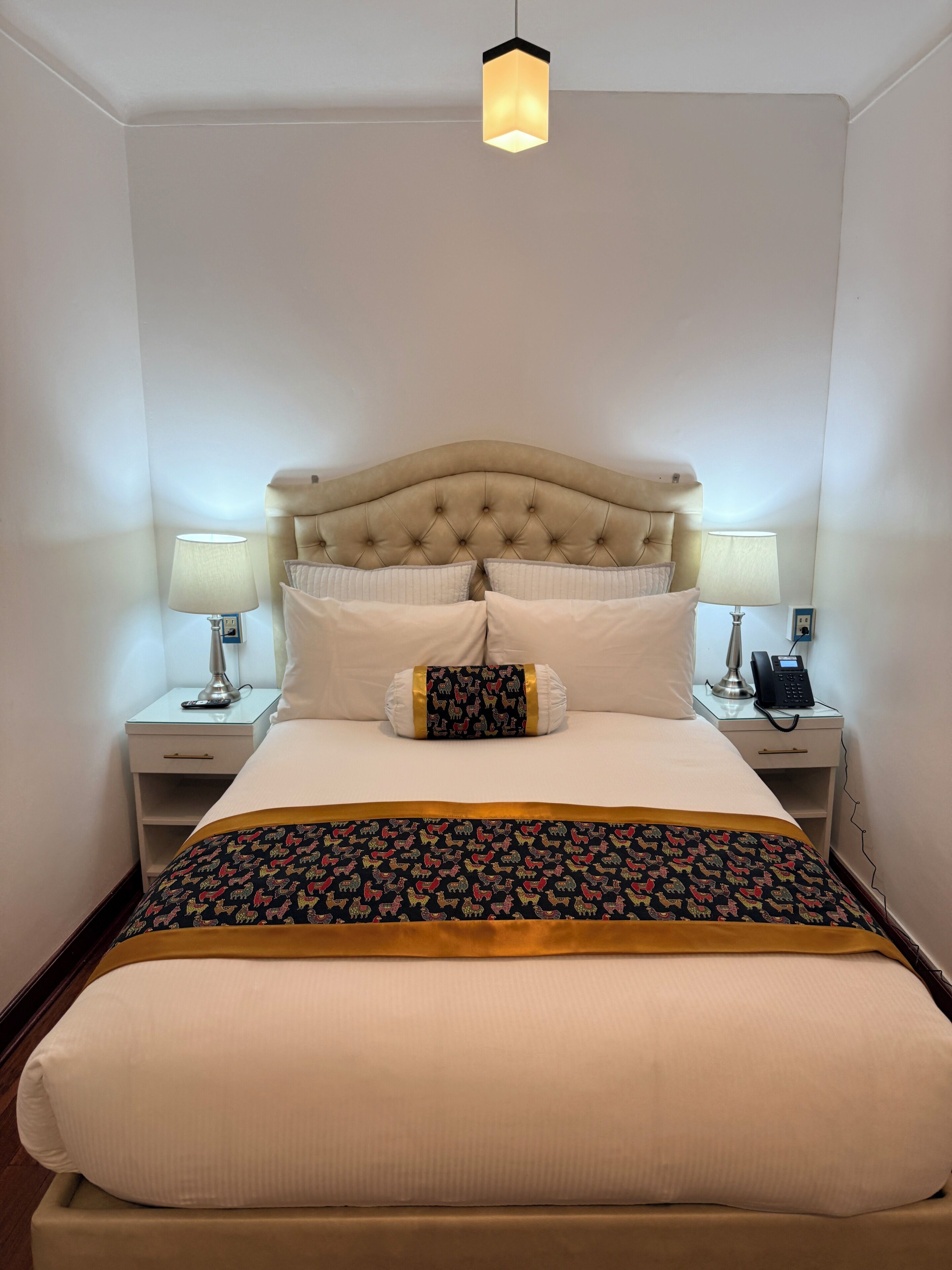 A neatly made bed with a tufted headboard, two bedside lamps, a telephone, and a patterned throw blanket.