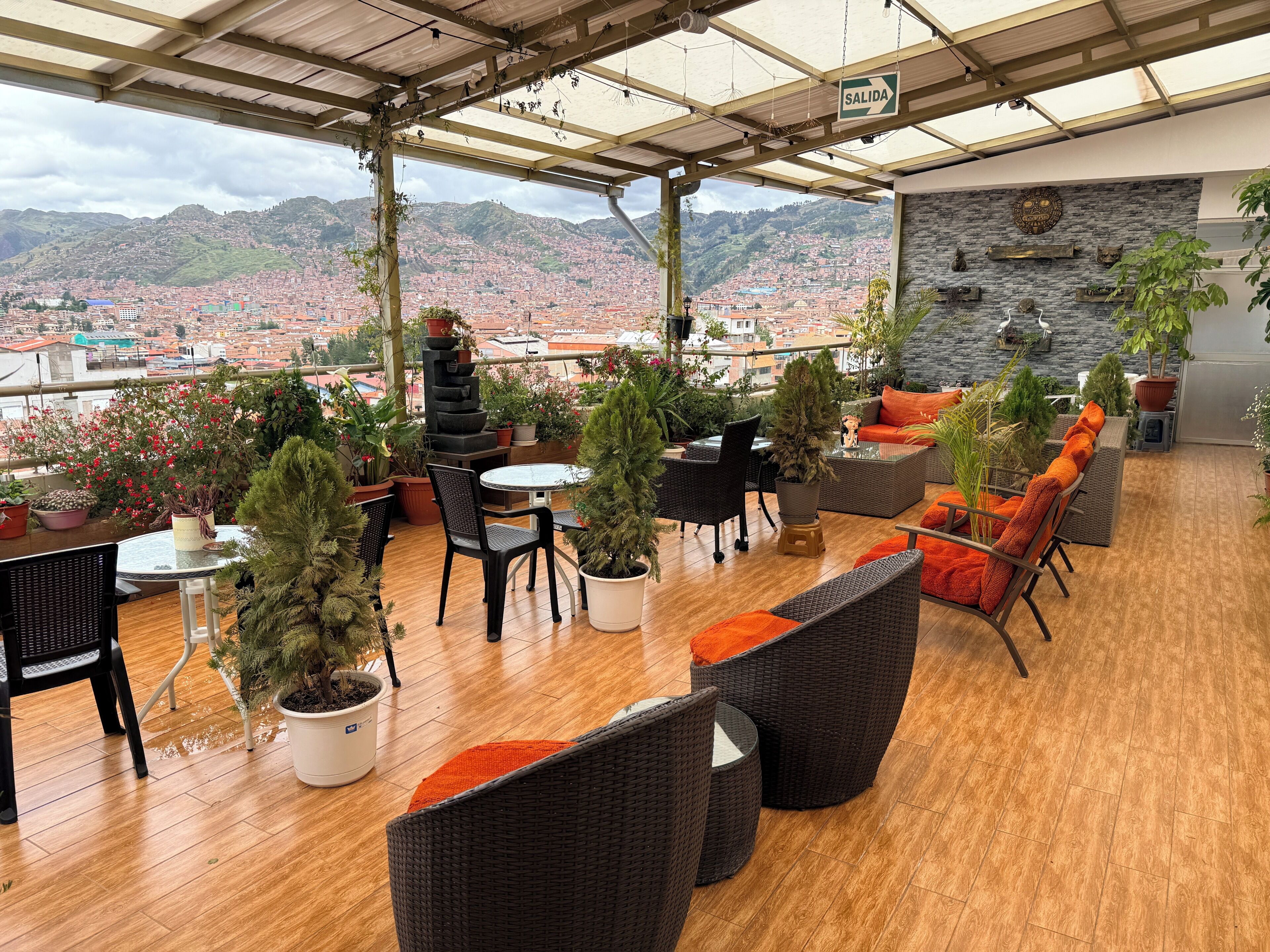 A covered outdoor seating area with potted plants, wicker furniture, and a view of a cityscape.