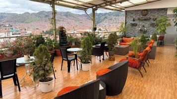 Un espace extérieur aménagé, abrité et doté de plantes en pot, de meubles en osier et offrant une vue sur le paysage urbain.