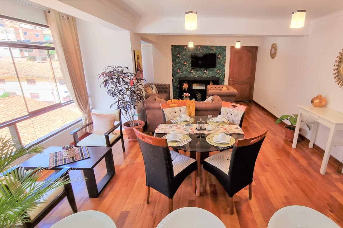 A furnished living room with a dining area, a fireplace, and a TV mounted on the wall.