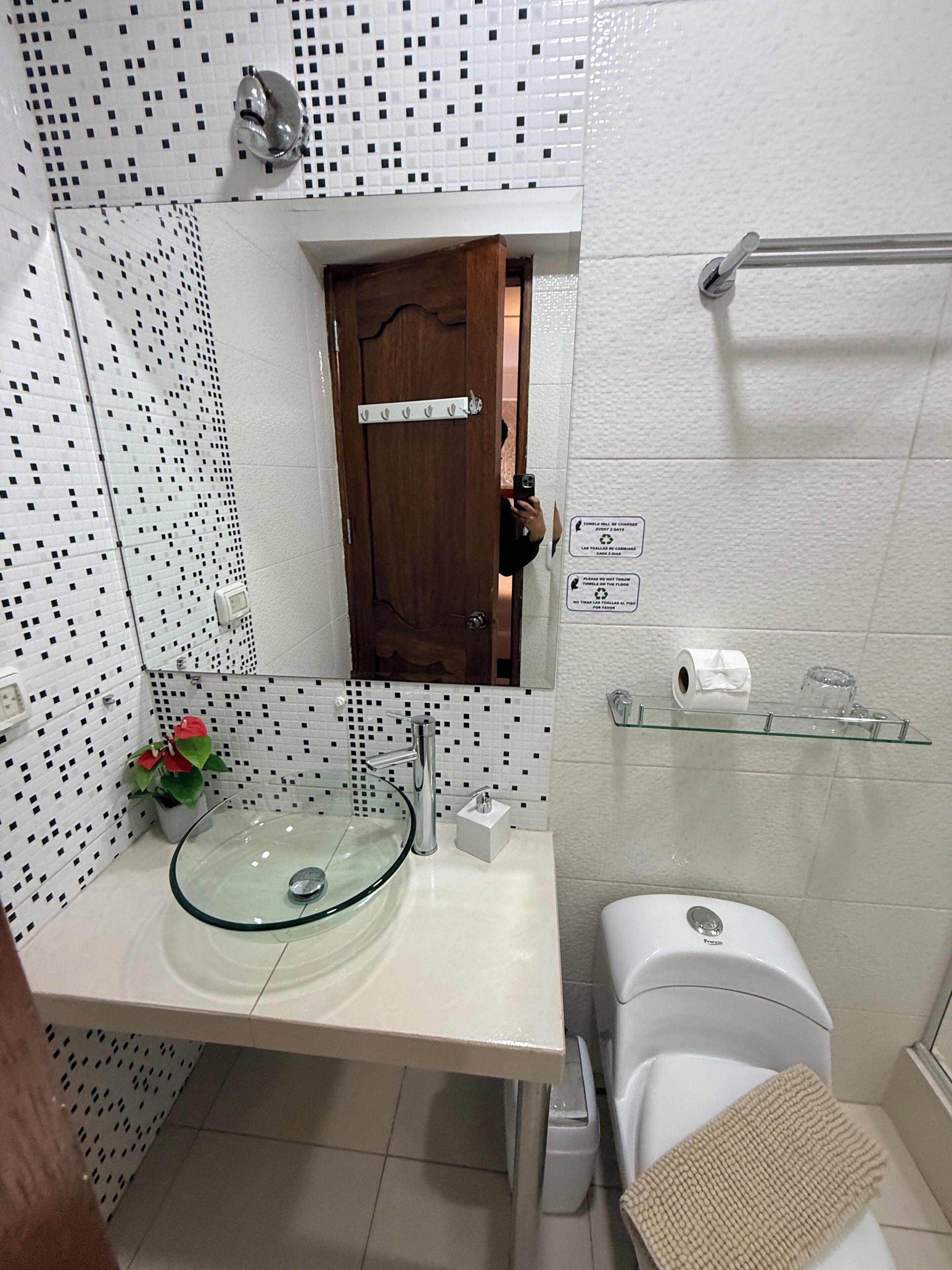 Une salle de bain avec un lavabo en verre, des toilettes, un espace douche et une petite étagère contenant des articles de toilette.