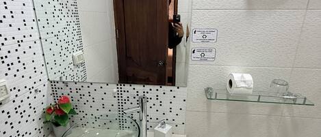 A bathroom with a glass sink, a toilet, a shower area, and a small shelf with toiletries.
