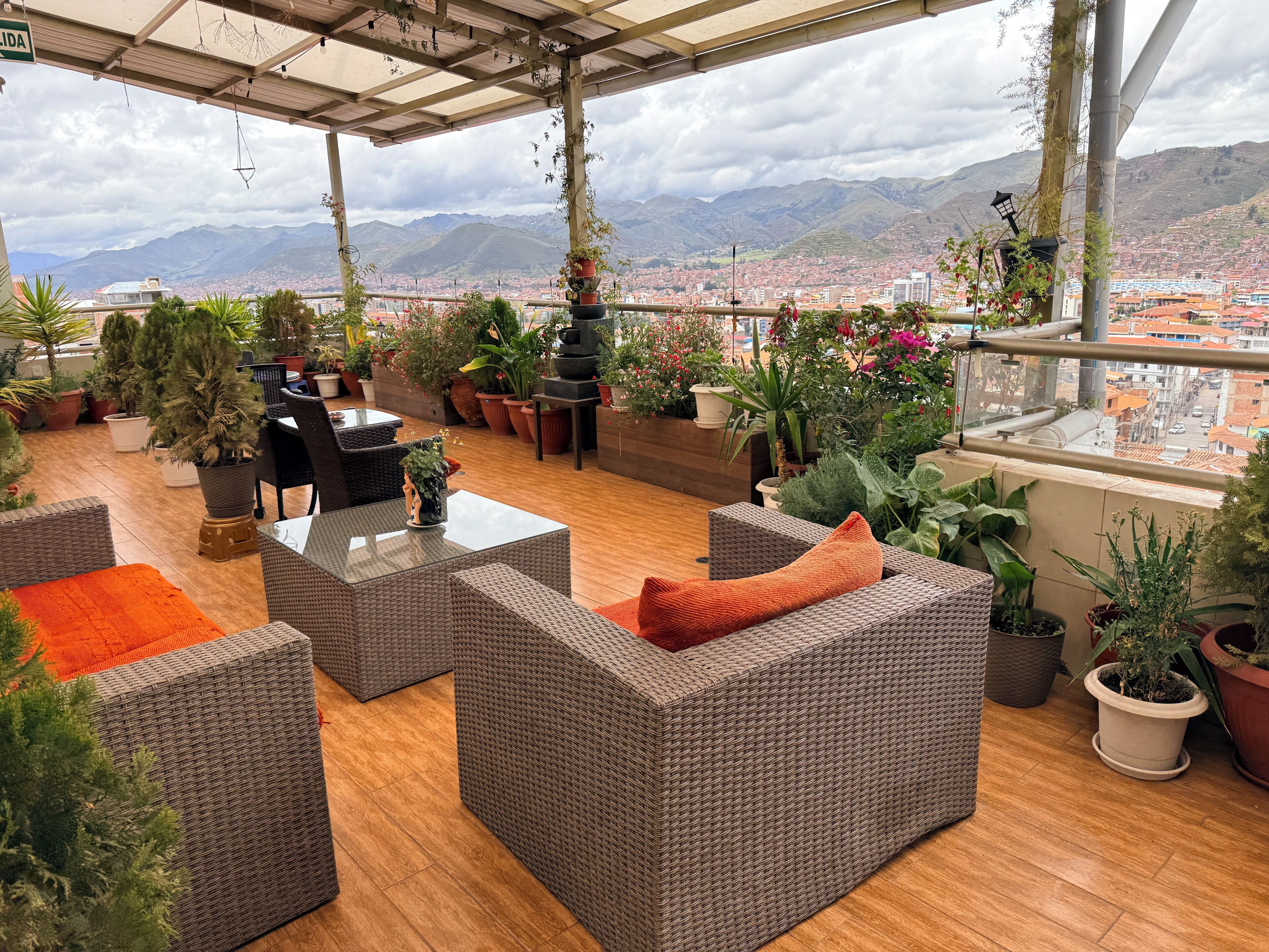 Terraço no telhado com mobiliário de vime, plantas em vasos e vista para a cidade.